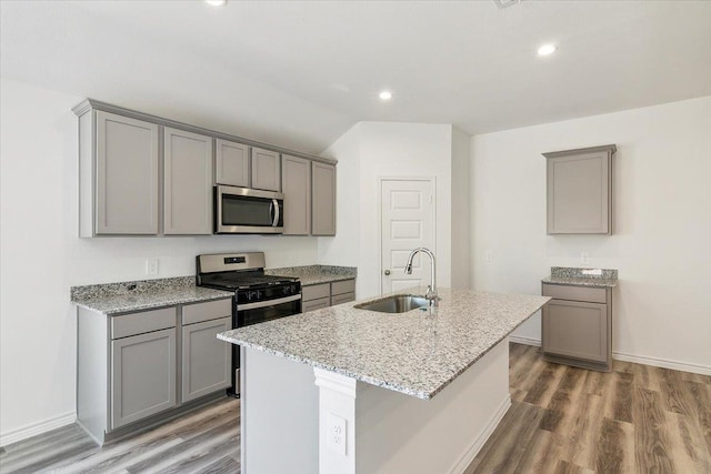 kitchen with light stone counters, stainless steel appliances, a kitchen island with sink, sink, and gray cabinets