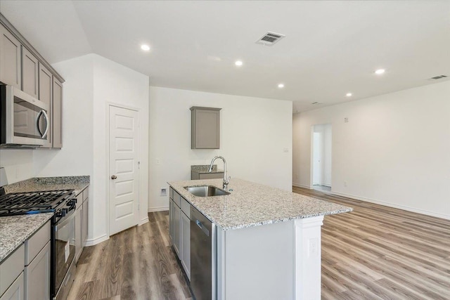 kitchen featuring sink, stainless steel appliances, light stone counters, gray cabinets, and a kitchen island with sink