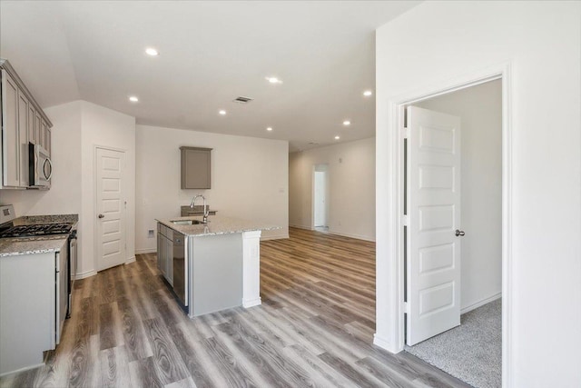 kitchen with sink, light stone counters, gray cabinets, a kitchen island with sink, and appliances with stainless steel finishes