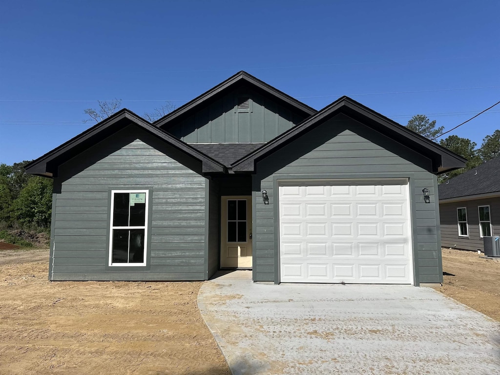 view of front of property featuring driveway, central AC, board and batten siding, and an attached garage