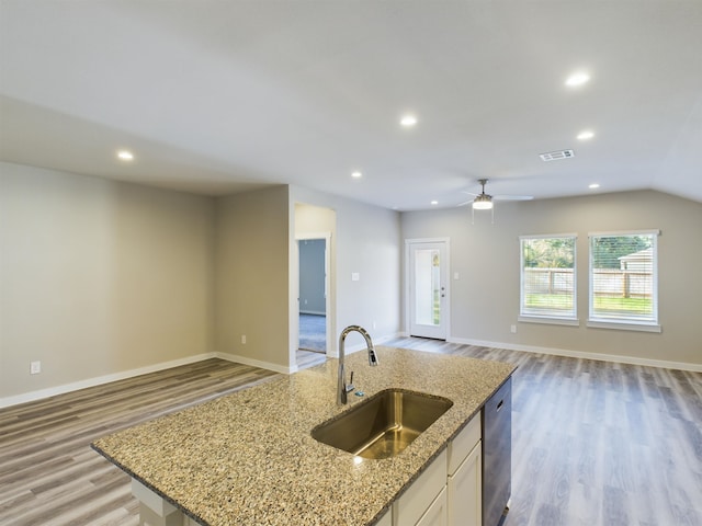 kitchen with white cabinets, a center island with sink, sink, light hardwood / wood-style floors, and light stone counters