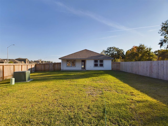 rear view of house with central AC and a yard