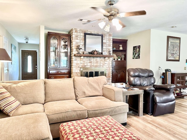 living room featuring a fireplace, a textured ceiling, light hardwood / wood-style floors, and ceiling fan