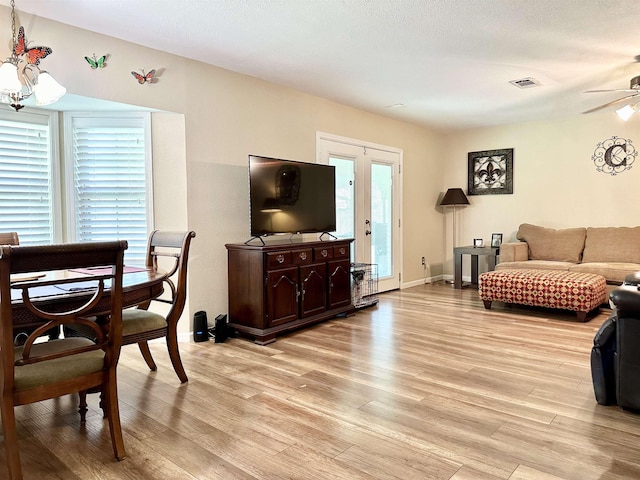 living room with french doors, ceiling fan with notable chandelier, light hardwood / wood-style flooring, and plenty of natural light