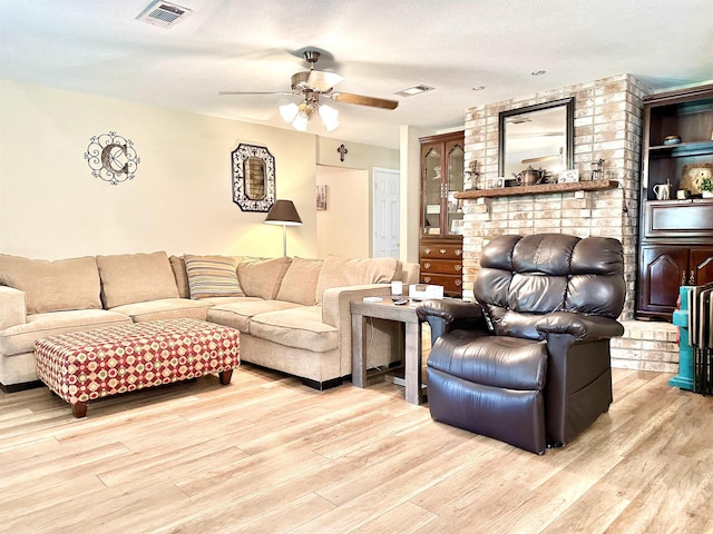 living room with ceiling fan, light wood-type flooring, and a textured ceiling