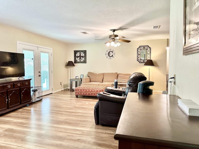 living room featuring ceiling fan, light hardwood / wood-style floors, a textured ceiling, and french doors