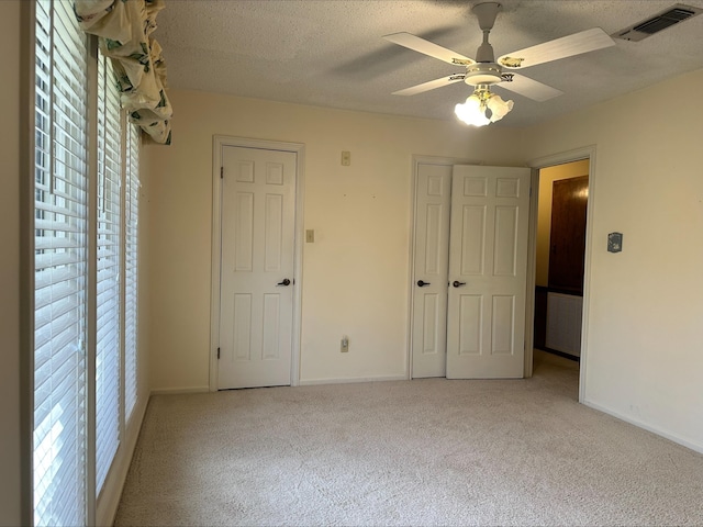 unfurnished bedroom with ceiling fan, light colored carpet, and a textured ceiling