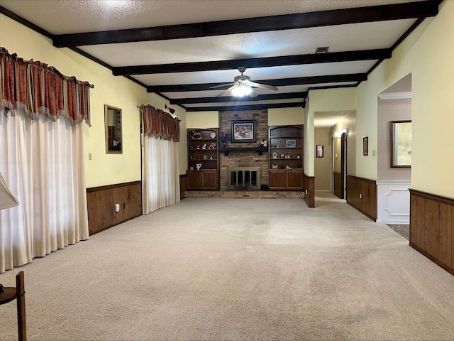 living room with wooden walls, a textured ceiling, a brick fireplace, light colored carpet, and beamed ceiling