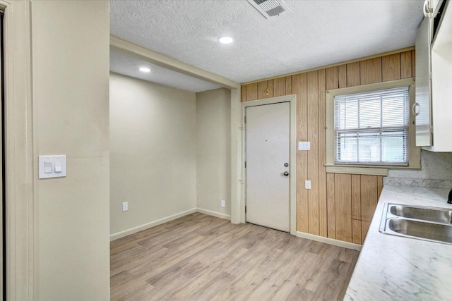 kitchen with wooden walls, sink, light hardwood / wood-style floors, and a textured ceiling