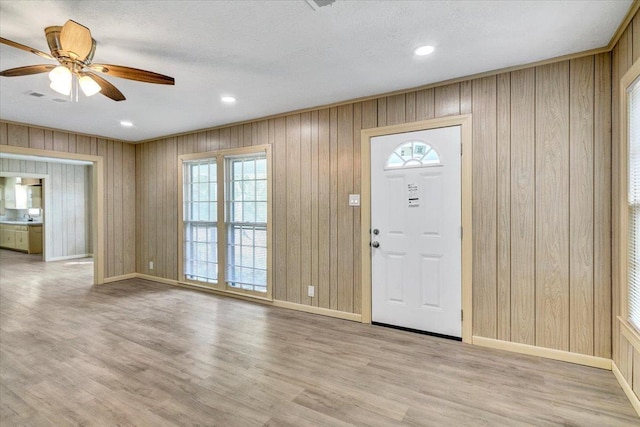 foyer entrance featuring a textured ceiling, light wood-type flooring, ceiling fan, and wood walls