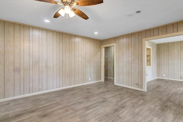 empty room with hardwood / wood-style floors, ceiling fan, and wooden walls