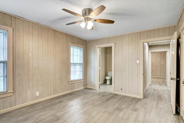 interior space featuring wood walls, ceiling fan, light hardwood / wood-style floors, and a textured ceiling