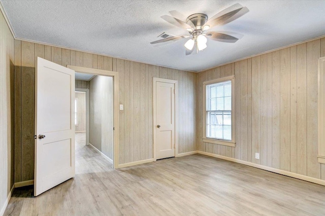 unfurnished bedroom with a textured ceiling, light hardwood / wood-style flooring, ceiling fan, and wood walls