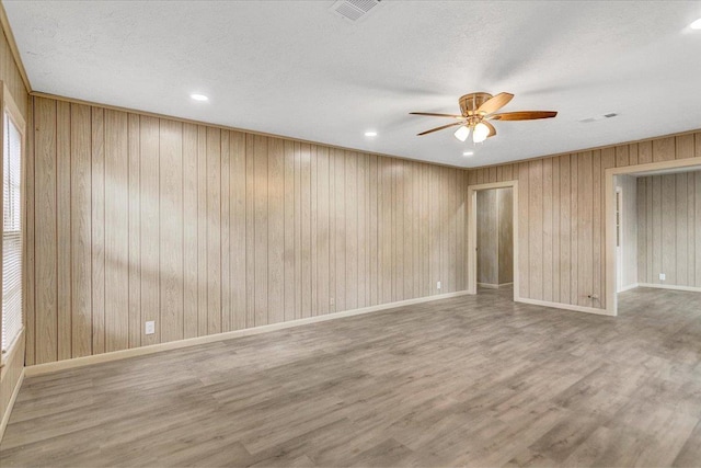 spare room featuring ceiling fan, a textured ceiling, wooden walls, and light hardwood / wood-style flooring