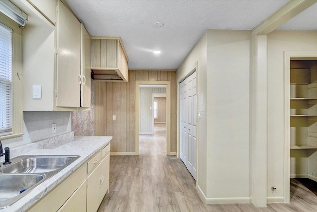 kitchen with wood walls, cream cabinets, sink, light wood-type flooring, and a textured ceiling