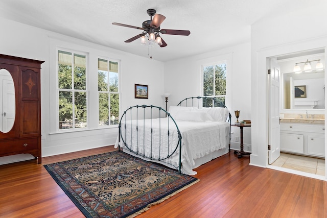 bedroom with multiple windows, hardwood / wood-style floors, ensuite bath, and ceiling fan