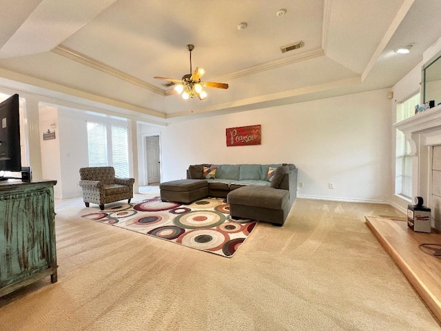 living area featuring visible vents, a raised ceiling, a ceiling fan, light colored carpet, and ornamental molding