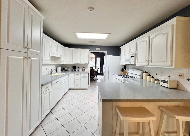 kitchen featuring a peninsula, white appliances, a kitchen breakfast bar, white cabinets, and light countertops