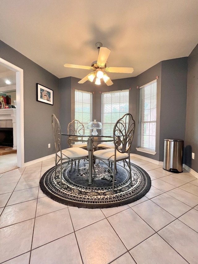 dining space with light tile patterned floors, ceiling fan, a tiled fireplace, and baseboards