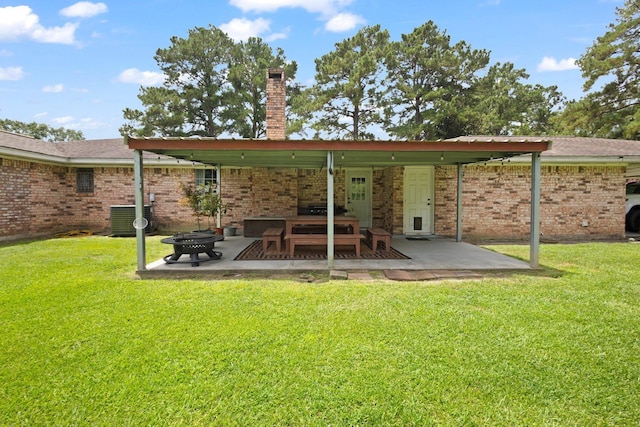 4169 Leatherwood Dr, Kountze, TX 77625 - back of property featuring a chimney, a lawn, a patio area, an outdoor fire pit, and brick siding