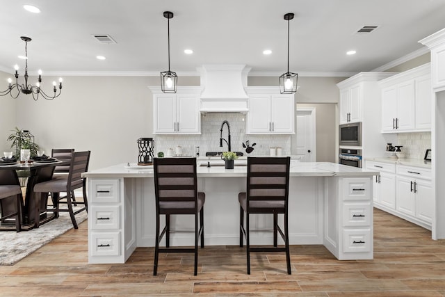 kitchen with decorative light fixtures, an island with sink, and premium range hood