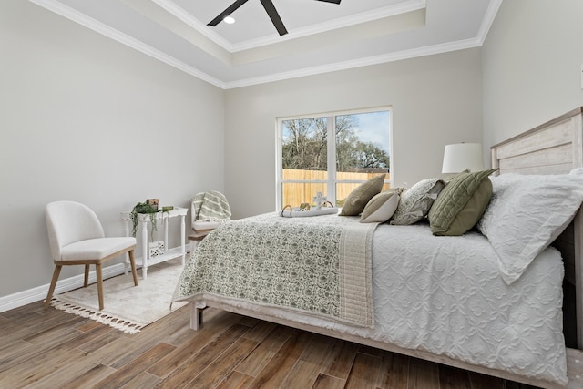 bedroom featuring hardwood / wood-style flooring, ornamental molding, ceiling fan, and a tray ceiling