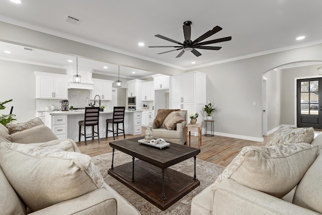 living room featuring ceiling fan, ornamental molding, sink, and light wood-type flooring