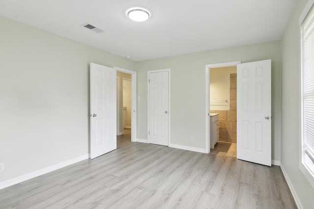 unfurnished bedroom featuring ensuite bath, a closet, and light hardwood / wood-style flooring