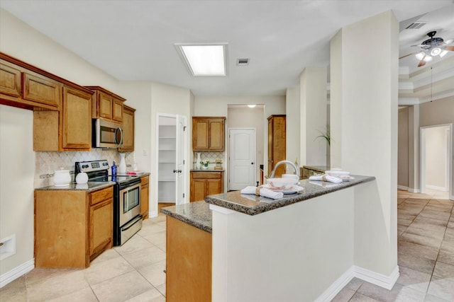 kitchen featuring backsplash, ceiling fan, dark stone countertops, kitchen peninsula, and stainless steel appliances