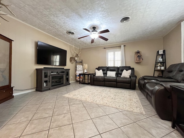 living room with ceiling fan, crown molding, light tile patterned floors, and a fireplace