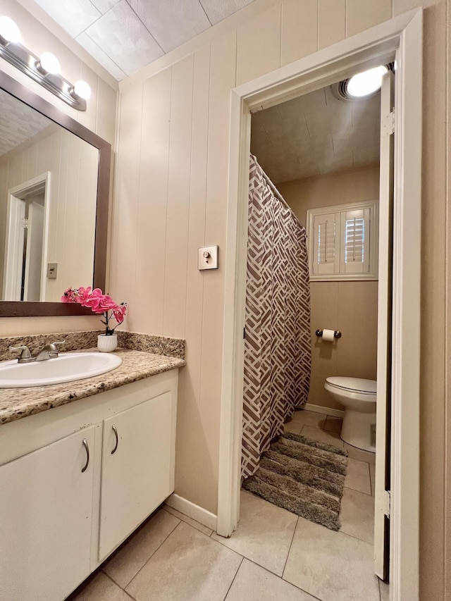 bathroom with tile patterned flooring, vanity, wood walls, and toilet