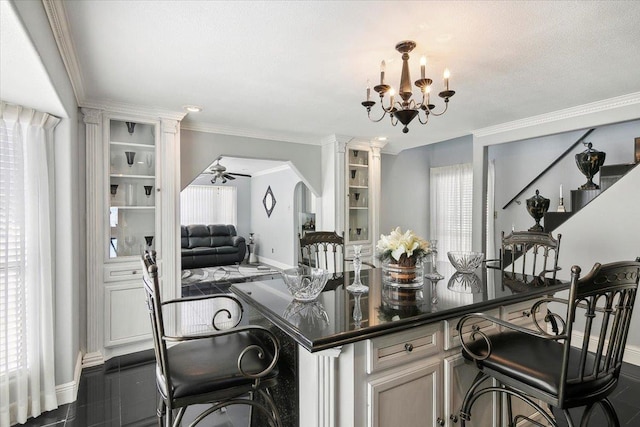 kitchen with ceiling fan with notable chandelier, ornamental molding, a breakfast bar area, and a wealth of natural light