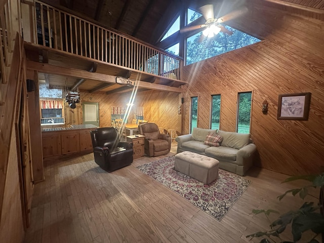 living area featuring wooden walls, a ceiling fan, light wood-style floors, a wealth of natural light, and high vaulted ceiling