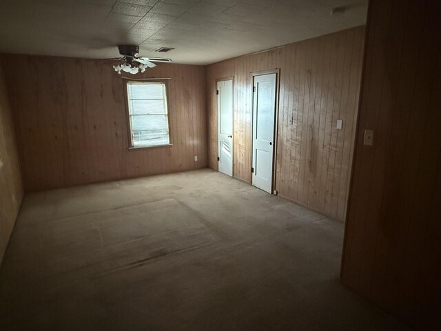 unfurnished bedroom with ceiling fan, wood walls, and light carpet