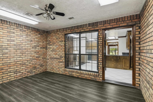 empty room featuring ceiling fan, a textured ceiling, brick wall, and dark wood-type flooring