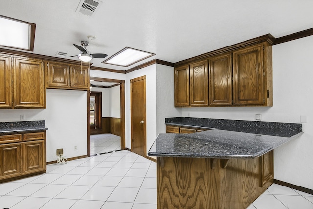 kitchen with kitchen peninsula, ceiling fan, crown molding, light tile patterned floors, and dark stone countertops