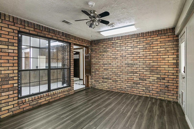 spare room with ceiling fan, dark hardwood / wood-style floors, a textured ceiling, and brick wall