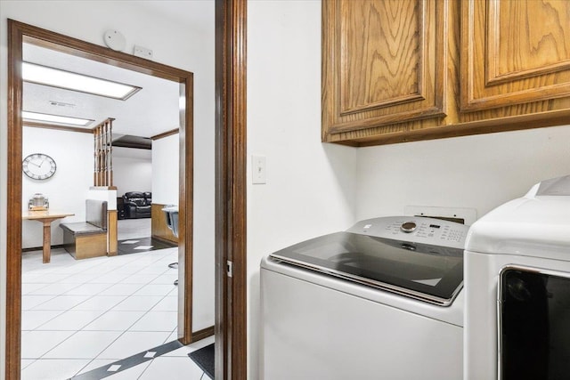 washroom with light tile patterned flooring, cabinets, and washing machine and clothes dryer