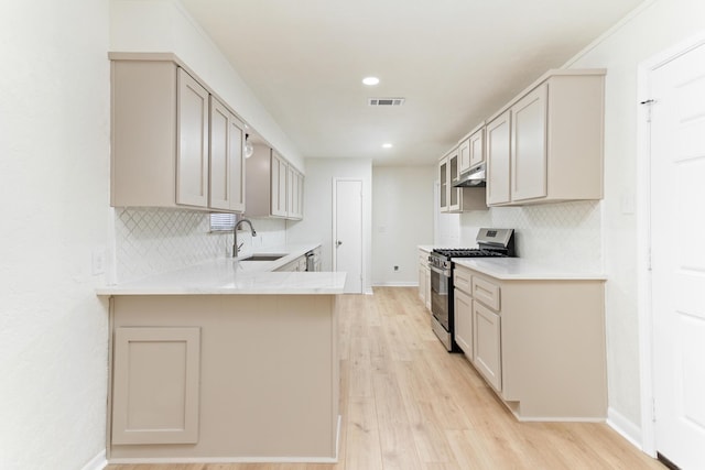 kitchen featuring kitchen peninsula, tasteful backsplash, stainless steel gas range, sink, and light hardwood / wood-style floors