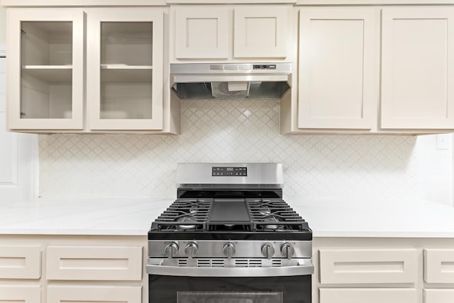 kitchen with decorative backsplash, light stone countertops, stainless steel gas range oven, and exhaust hood