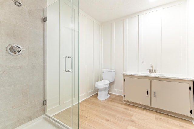 bathroom featuring a shower with door, vanity, hardwood / wood-style floors, and toilet