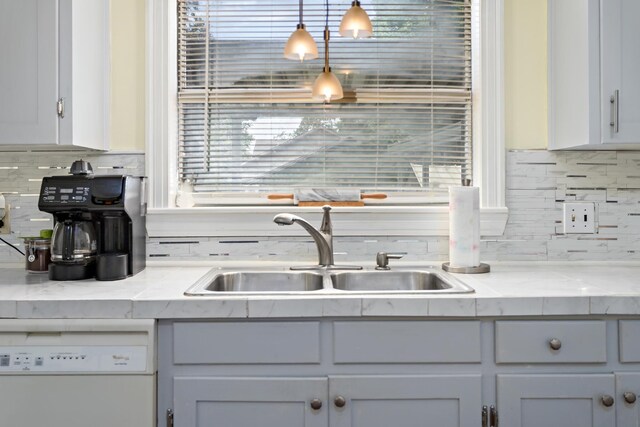 kitchen with light stone countertops, white cabinets, sink, decorative light fixtures, and dishwasher