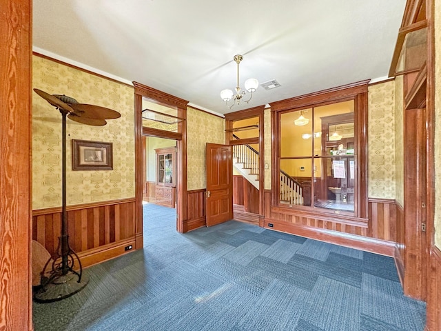 carpeted spare room featuring a notable chandelier and crown molding