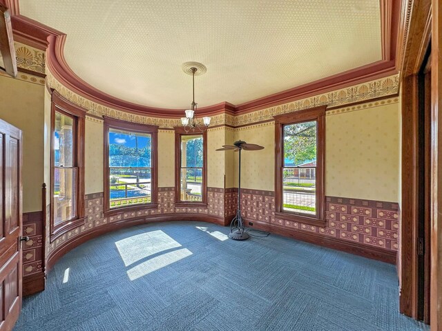 spare room with dark colored carpet, ceiling fan with notable chandelier, and ornamental molding