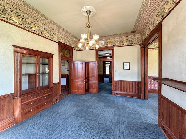 interior space featuring dark colored carpet, wood walls, and an inviting chandelier