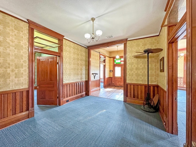 spare room with a chandelier, a textured ceiling, carpet flooring, and crown molding