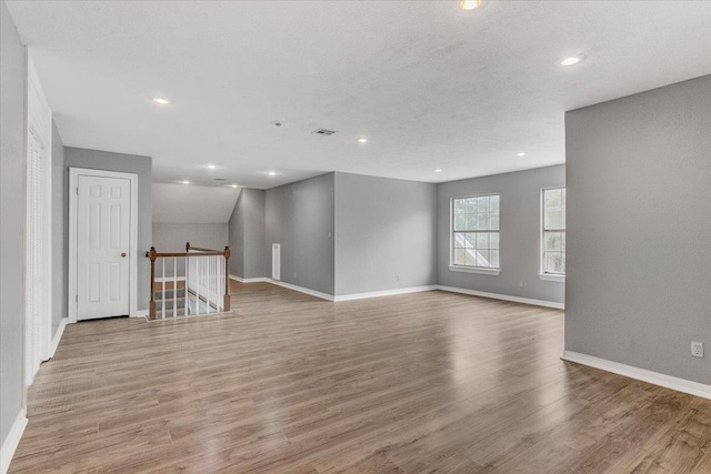 empty room featuring a textured ceiling, light hardwood / wood-style floors, and vaulted ceiling