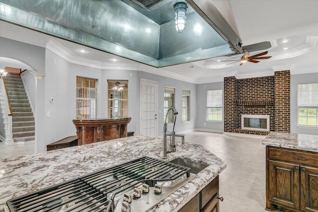 kitchen with ceiling fan, a brick fireplace, decorative columns, crown molding, and stainless steel gas stovetop