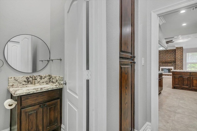 bathroom featuring crown molding, tile patterned flooring, vanity, and a brick fireplace