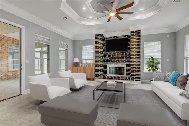 living room featuring a brick fireplace, brick wall, a tray ceiling, ceiling fan, and crown molding